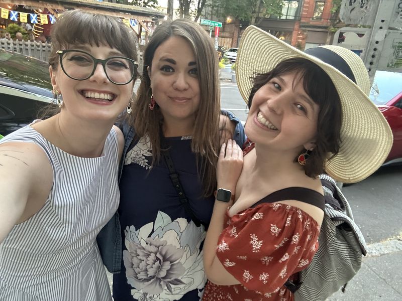 Ashley taking a selfie with two friends on a city street, all three smiling.