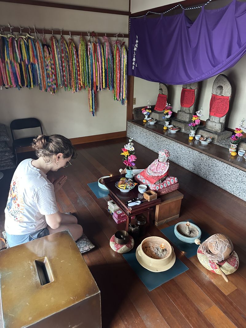 Ashley sitting quietly in a small temple room hung with strings of colorful paper cranes.