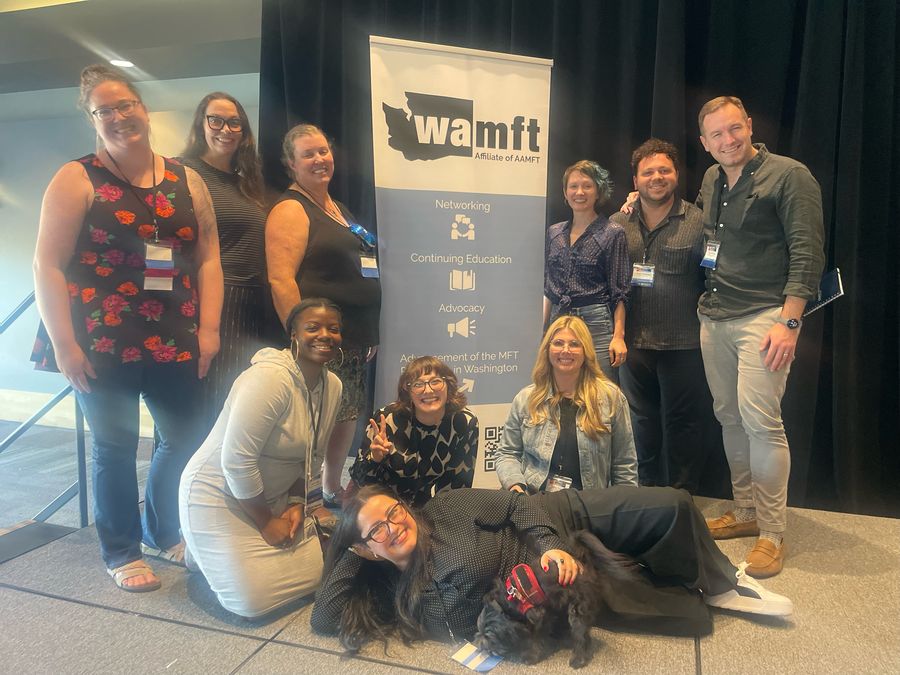 Ashley with a group of fellow marriage and family therapists in front of a WAMFT banner, one of them lying on the floor with a small black dog.